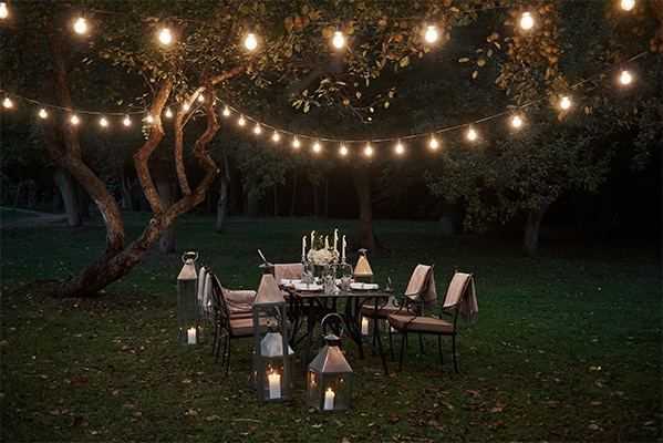 String lights hanging over an outdoor dining area in a garden at night, creating a warm and inviting atmosphere.